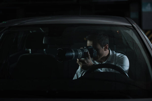 частный детектив-мужчина шпионит на камеру со стеклом из своей машины
