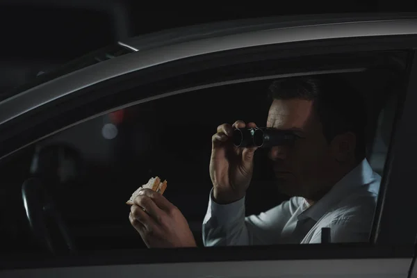 Masculino Detetive Privado Fazendo Vigilância Por Binóculos Comer Sanduíche Carro — Fotografia de Stock