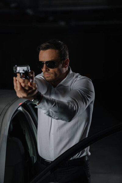 front view of undercover male agent in sunglasses aiming by gun 