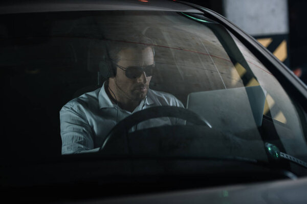 focused male private detective in headphones doing surveillance with laptop in car