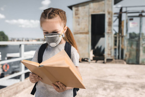 kid in protective mask reading book on bridge, air pollution concept