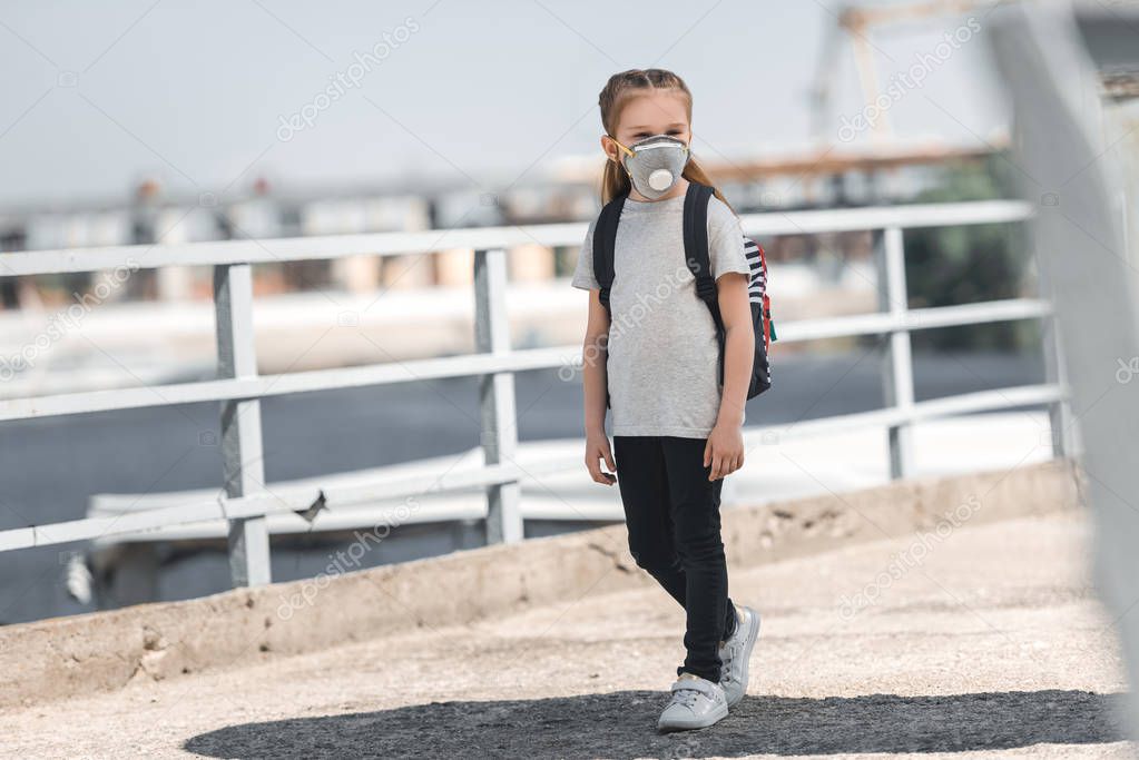 child in protective mask walking on bridge, air pollution concept