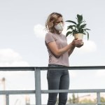 Femme en masque de protection tenant la plante verte en pot sur le pont, concept de pollution atmosphérique