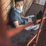 High angle view of asian teen in protective mask sitting with laptop on staircase, air pollution concept