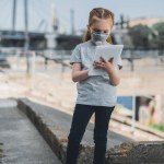 Criança em máscara protetora usando tablet na rua, conceito de poluição do ar