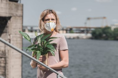 woman in protective mask holding potted plant on bridge, air pollution concept clipart