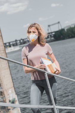 woman in protective mask standing on bridge with books, air pollution concept clipart