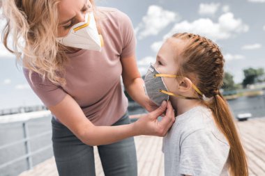 mother wearing protective mask on daughter on bridge, air pollution concept