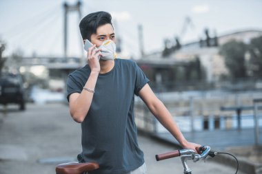 smartphone ile konuşmak ve bisiklet üzerinde hava kirliliği kavramı eğilerek koruyucu maske içinde Asya teen