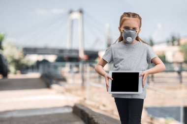 child in protective mask showing tablet on street, air pollution concept clipart