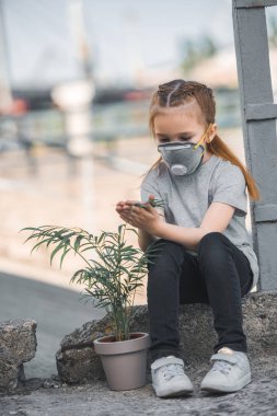 child in protective mask touching green potted plant, air pollution concept clipart