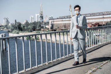 asian businessman in protective mask walking on bridge with coffee to go, air pollution concept clipart