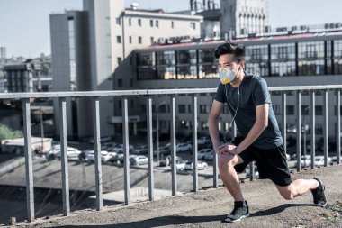 asian teen stretching legs in protective mask on bridge, air pollution concept clipart