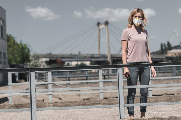 woman in protective mask standing on bridge, air pollution concept