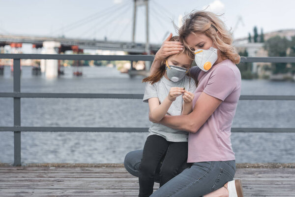 mother in protective mask hugging daughter on bridge, air pollution concept