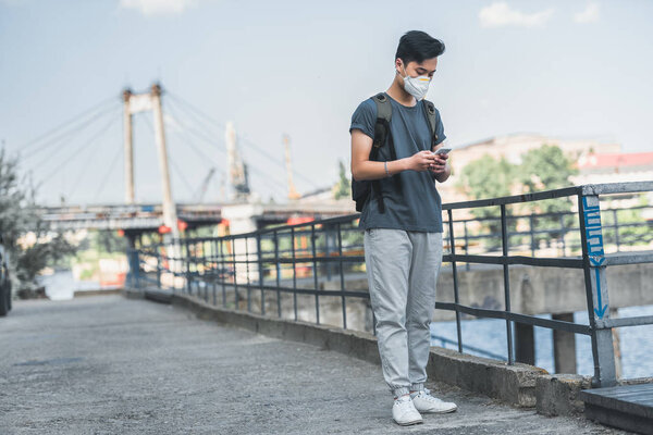 asian teen in protective mask using smartphone, air pollution concept