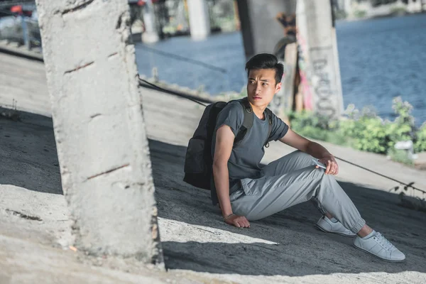 Asian Teenager Sitting Smartphone Looking Away Bridge City — Free Stock Photo