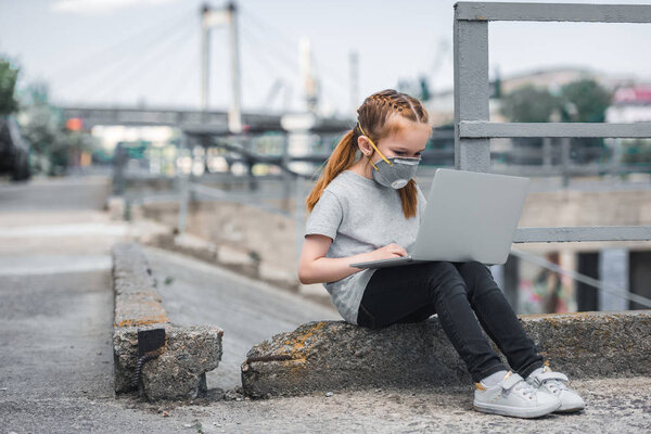 child in protective mask using laptop on street, air pollution concept