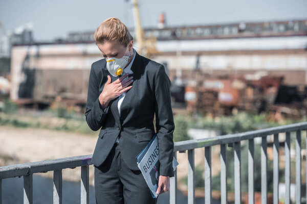 businesswoman in protective mask touching chest on bridge, air pollution concept