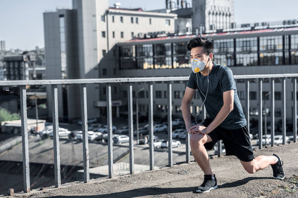 asian teen stretching legs in protective mask on bridge, air pollution concept