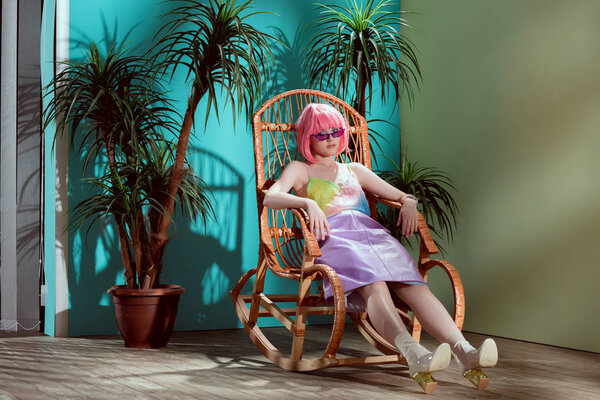 full length view of attractive stylish female model in pink wig sitting in rocking chair