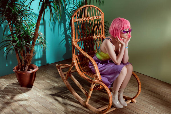 beautiful stylish girl in pink wig sitting in rocking chair and looking away