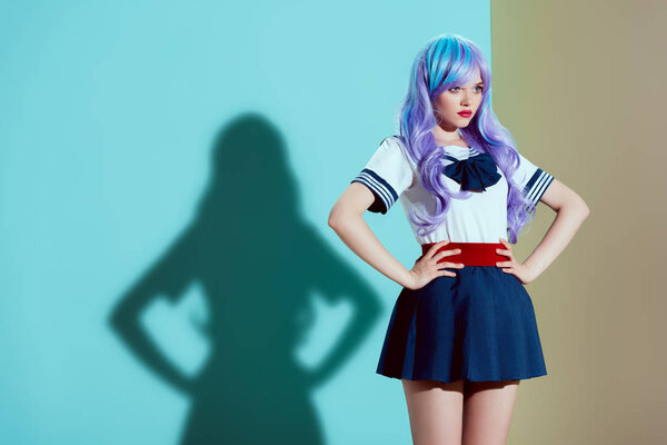 attractive stylish girl in bright wig and skirt standing with hands on waist and looking away in studio