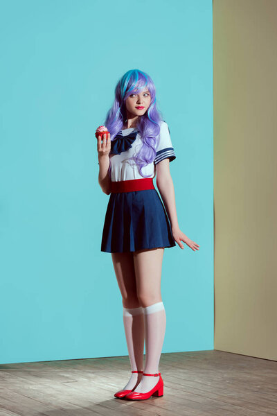 full length view of beautiful girl in bright wig holding sweet cupcake in studio