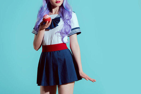cropped shot of girl in anime clothing holding delicious cupcake isolated on blue