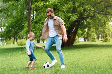 father and son having fun and playing football at park clipart
