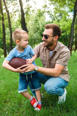 happy father and son with american football ball at park clipart