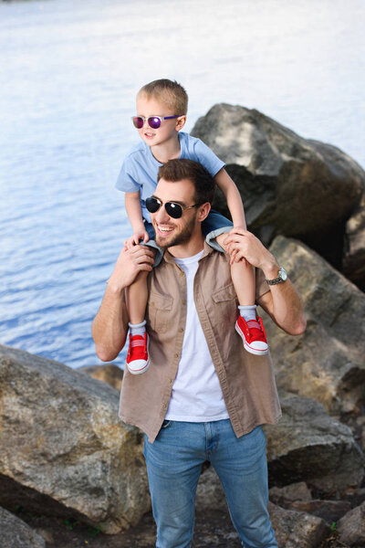 happy father holding son on shoulders and they looking away at park