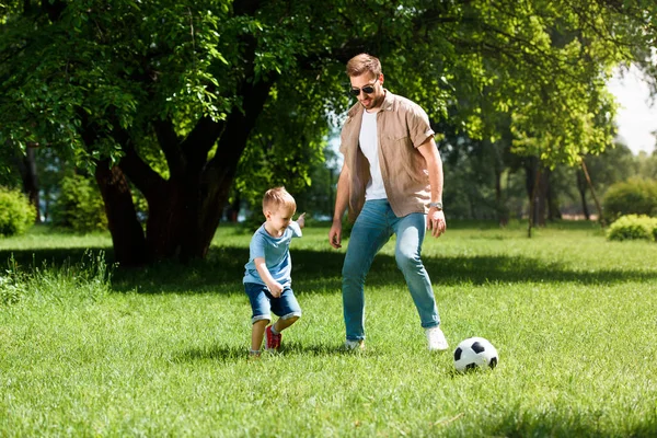 father and son playing football on grass at park