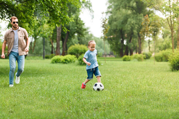 отец и сын вместе играют в футбол в парке
