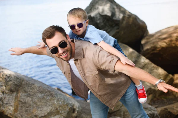 Happy father giving piggy back to son near lake at park — Stock Image Happy Father Giving Piggy Back Son Lake Park Stock Image