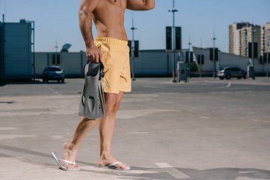 cropped shot of shirtless man in swimming shorts with flippers on parking clipart