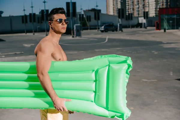 attractive young shirtless man with inflatable bed on parking