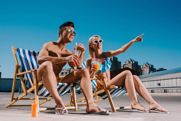 young couple with cocktails sitting on sun loungers on parking