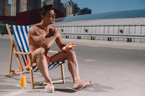 Όμορφος Νεαρός Άνδρας Shirtless Κάθονται Στην Ξαπλώστρα Και Εφαρμόζοντας Αντηλιακό — Δωρεάν Φωτογραφία