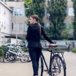 Rückansicht einer jungen Geschäftsfrau, die neben einem Retro-Fahrrad auf der Straße steht