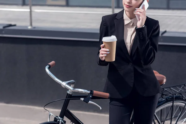 街のレトロな自転車の近くに立っている間フォンで話して行くにコーヒーと実業家の部分的なビュー  — 無料ストックフォト