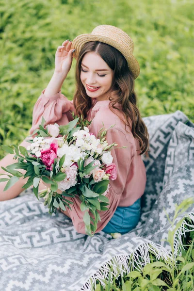beautiful smiling woman with bouquet of flowers resting on blanket in park