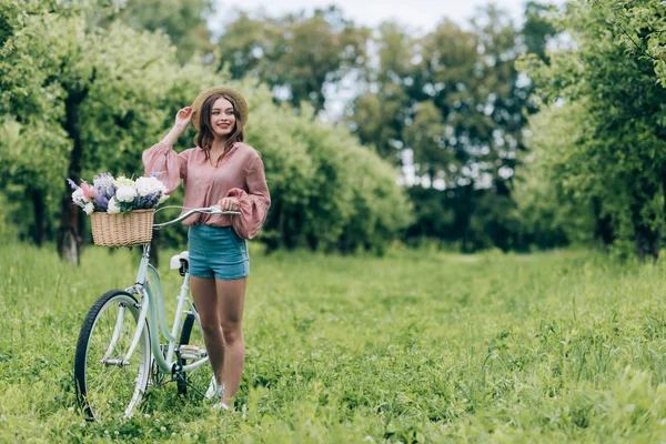 Young pretty woman holding retro bicycle with wicker basket full of flowers in forest — Stock Image Young Pretty Woman Holding Retro Bicycle Wicker Basket Full Flowers Stock Picture