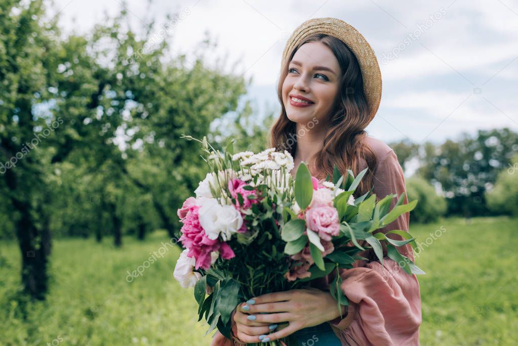 portrait of pretty young woman in hat with bouquet of flowers in park