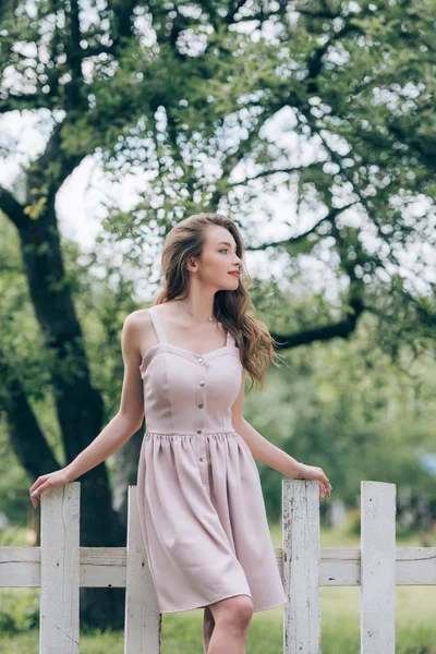 田舎で白いフェンスでスタイリッシュなドレスで物思いにふける美人 — ストック写真