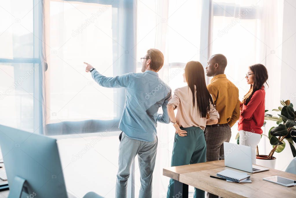 back view of multiethnic business colleagues looking out window in office