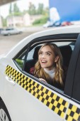 usměvavá mladá žena dívá oknem taxíku  