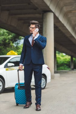 smartphone ile konuşmak ve uzak duran bavulu yakınındaki taksi ile seyir şık genç adam