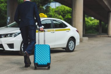 back view of young man with suitcase running to taxi cab clipart