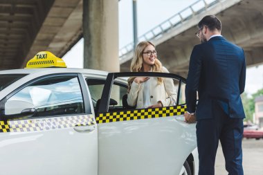 şık yakışıklı takside oturan gülümseyen sarışın kadın için arabanın kapısını açarak